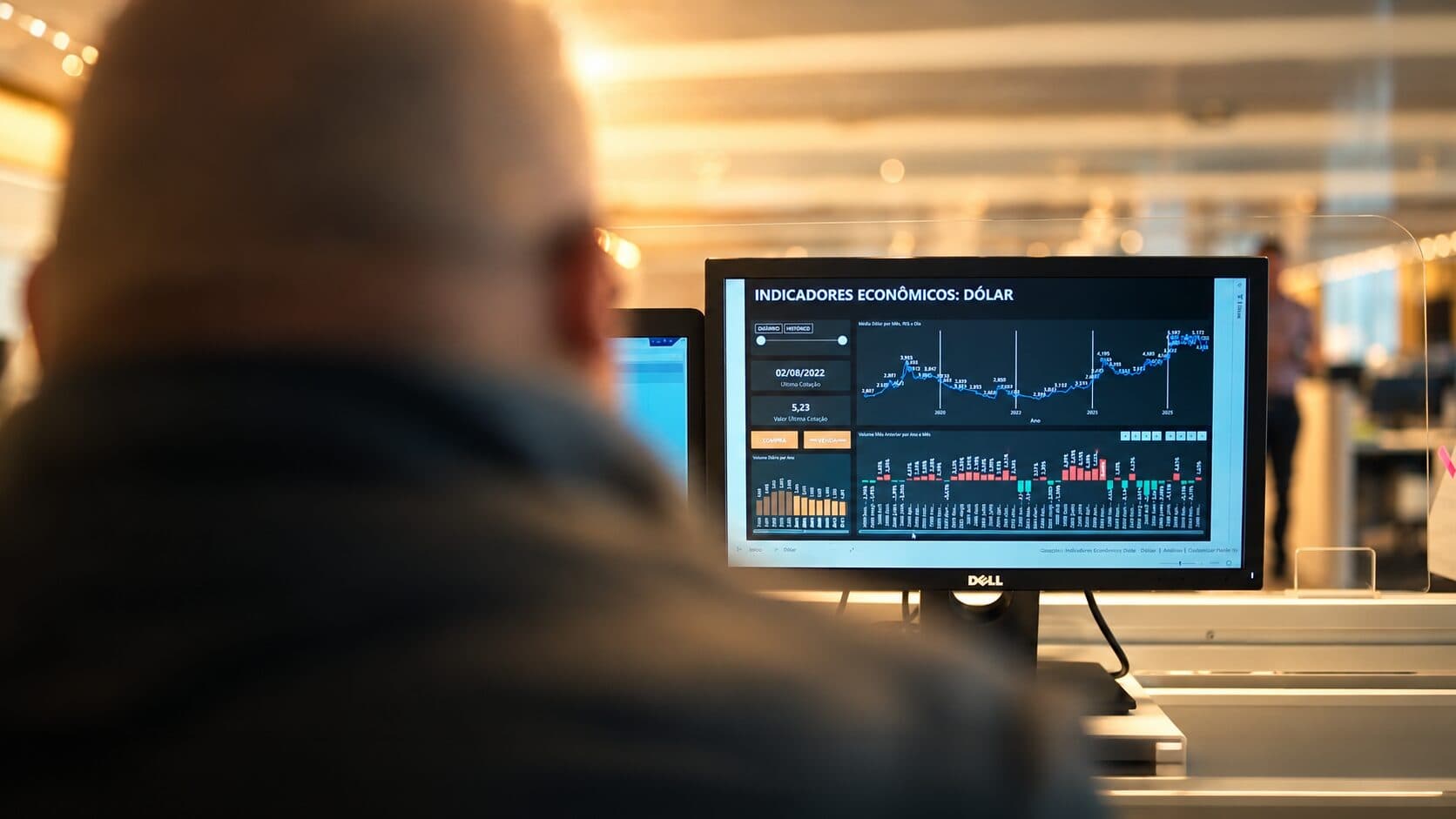 A professional seen from behind, facing a monitor with economic indicators